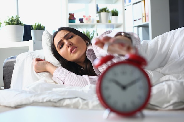 Une femme insatisfaite se trouve dans son lit et éteint le réveil