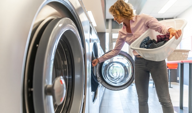 Femme insérant des vêtements sales dans la machine à laver dans la buanderie