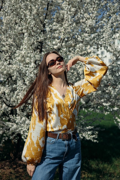 Femme insouciante aux cheveux longs profitant de la liberté au printemps contre un arbre en fleurs