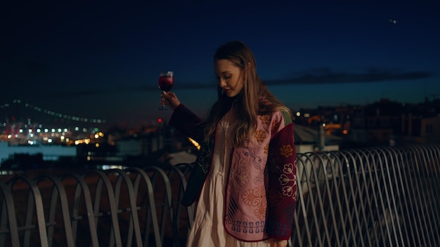 Une femme insouciante se détend un cocktail de vin se promène dans la rue en regardant le paysage urbain de nuit