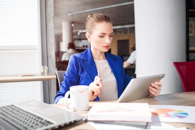 Une femme intelligente et belle est assise sur la table et regarde la tablette