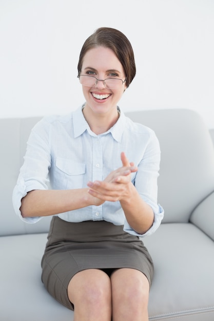 Femme intelligente souriante, frappant les mains sur le canapé