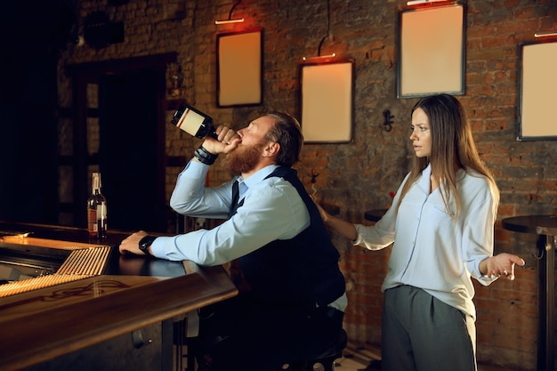 Une femme irritée gronde son mari ivre alors qu'il abuse de l'alcool au pub. Mauvaises habitudes et concept de dépendance