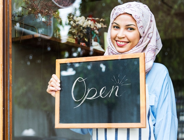 Femme islamique propriétaire de petite entreprise tenant tableau avec sourire