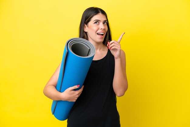 Femme italienne sportive allant à des cours de yoga isolés sur fond jaune en pensant à une idée pointant le doigt vers le haut