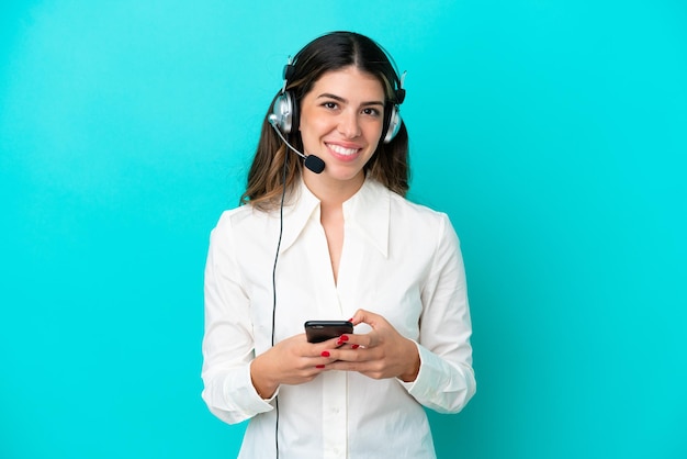 Femme italienne de télévendeur travaillant avec un casque isolé sur fond bleu envoyant un message avec le mobile