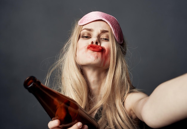 Une femme ivre avec une bouteille de bière sur un fond gris fait des gestes avec ses mains et un maquillage brillant Photo de haute qualité