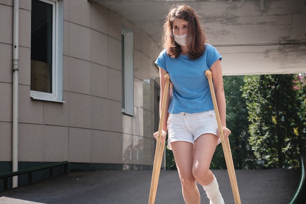 Une femme avec une jambe cassée descend une rampe à l'aide de béquilles orthopédiques.