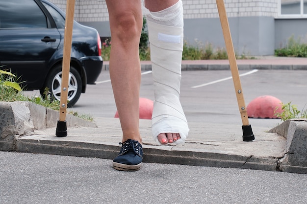 Une femme avec une jambe cassée surmonte un obstacle avec des béquilles.