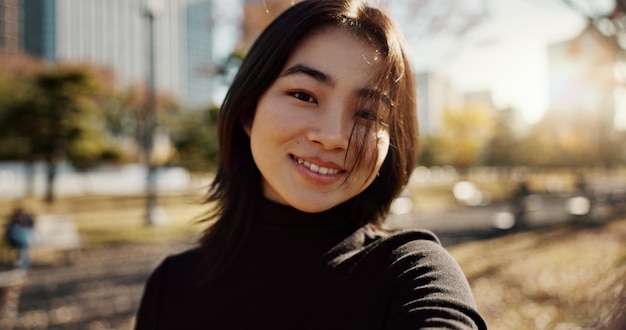 Femme japonaise heureuse et portrait dans le parc nature et chemin avec soleil ville et bâtiments avec fierté fille personne et sourire par la pelouse herbe et arbres dans le métro urbain en plein air et voyager à Tokyo