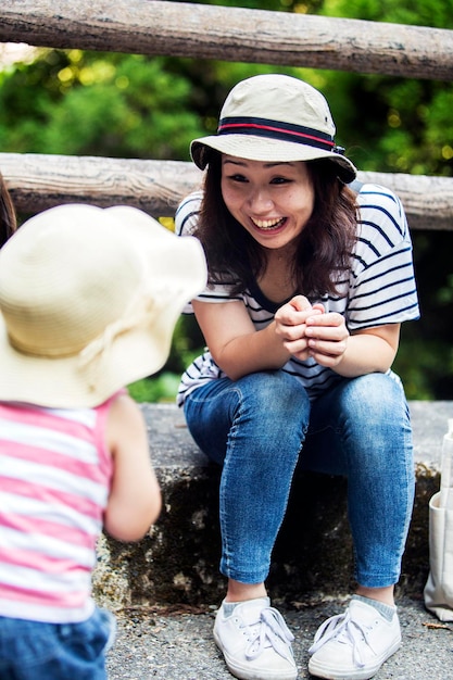Femme japonaise souriante parlant à une petite fille portant un chapeau de soleil, un haut rayé et un jean