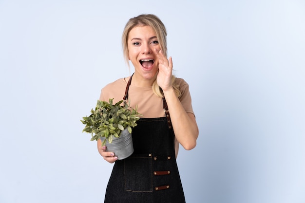 Femme de jardinier blonde tenant une plante en criant avec la bouche grande ouverte