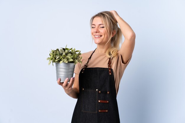 Femme de jardinier blonde tenant une plante sur un mur isolé en riant