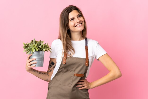 Femme de jardinier tenant une plante isolée sur fond rose posant avec les bras à la hanche et souriant