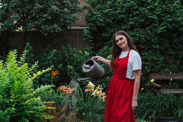 Une femme jardinière dans un tablier rouge arrosant le jardin