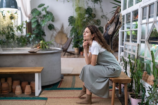 Femme jardinière se reposant après le travail dans un magasin de fleurs ou une serre rêvant et regardant par la fenêtre