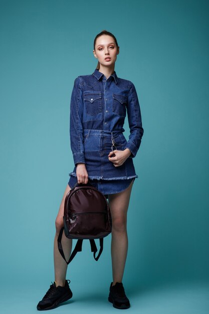 Femme en jean denim robe sneakersbackpack noir sur fond bleu turquoise Studio Shot