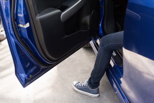 Une femme en jeans et chaussures de sport s'asseoir sur une voiture bleue avec porte ouverte