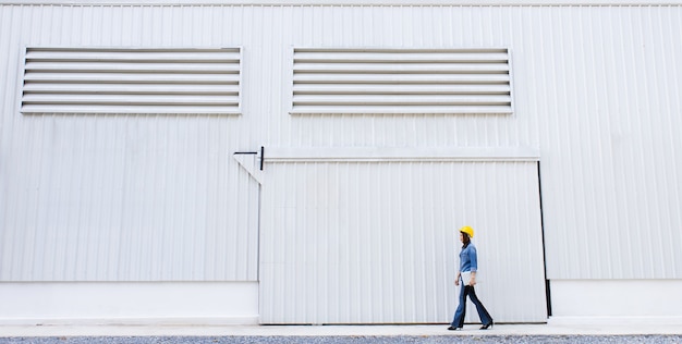 Femme en jeans portant un chapeau de sécurité jaune avant de la paroi en tôle au chantier de construction