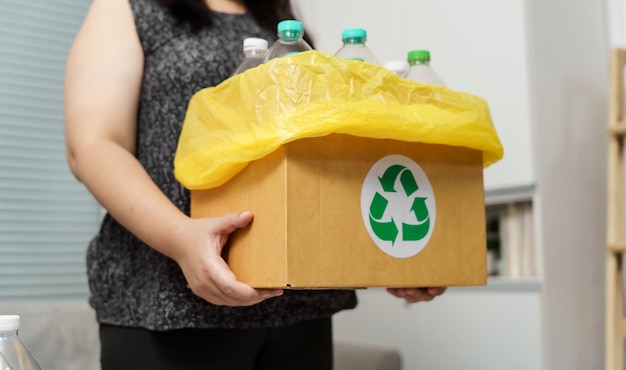 Femme jetant une bouteille en plastique vide dans la poubelle de recyclage avec des sacs à ordures jaunes à la maison