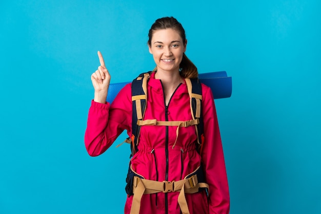 Femme jeune alpiniste sur mur bleu isolé pointant vers le haut une excellente idée