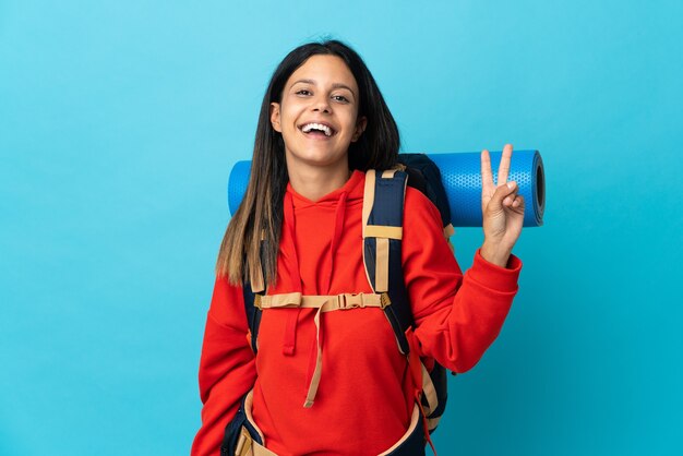 Femme jeune alpiniste avec sac à dos souriant et montrant le signe de la victoire