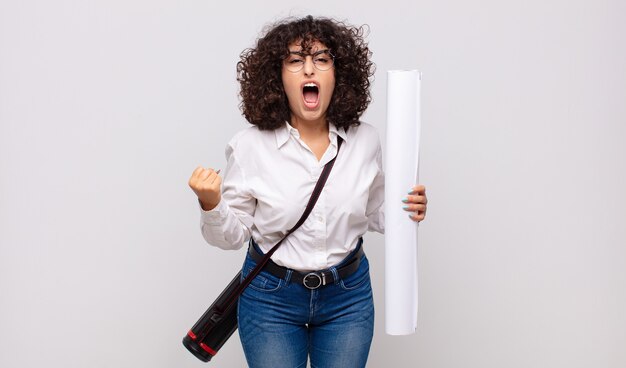 Femme jeune architecte criant de manière agressive avec une expression de colère ou les poings serrés célébrant le succès