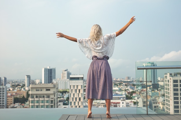 Femme jeune belle sur le toit de l'hôtel au bord de la piscine avec vue sur la ville