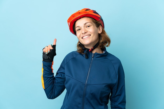 Femme jeune cycliste isolée sur mur bleu montrant et levant un doigt en signe de la meilleure