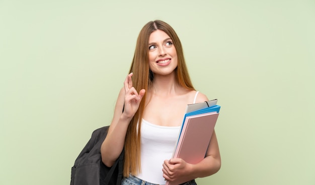 Femme jeune étudiant sur un mur vert isolé avec les doigts qui se croisent