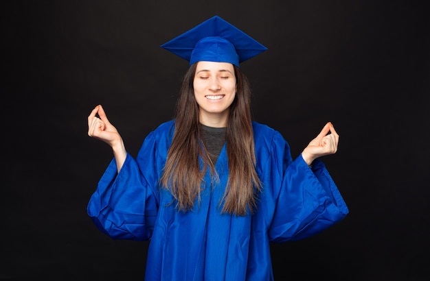 Femme jeune étudiante pacifique portant baccalauréat et chapeau et faisant un geste zen