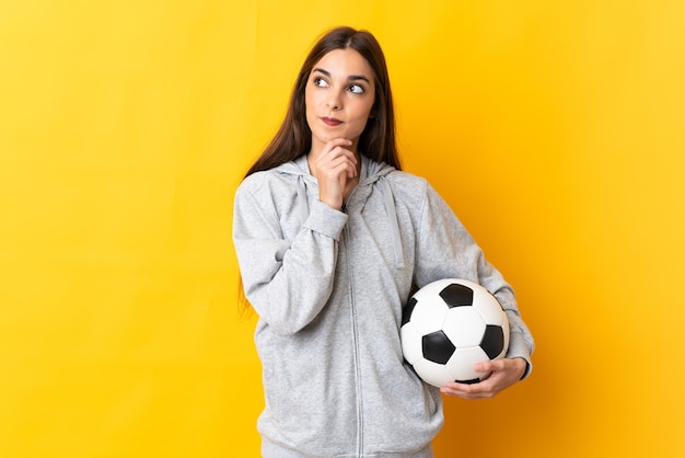 Femme jeune joueur de football isolé sur jaune pensant une idée tout en levant les yeux