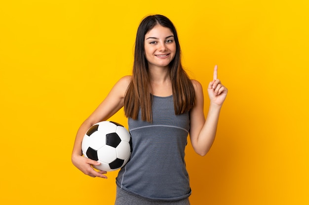Femme jeune joueur de football isolée sur un mur jaune pointant vers le haut