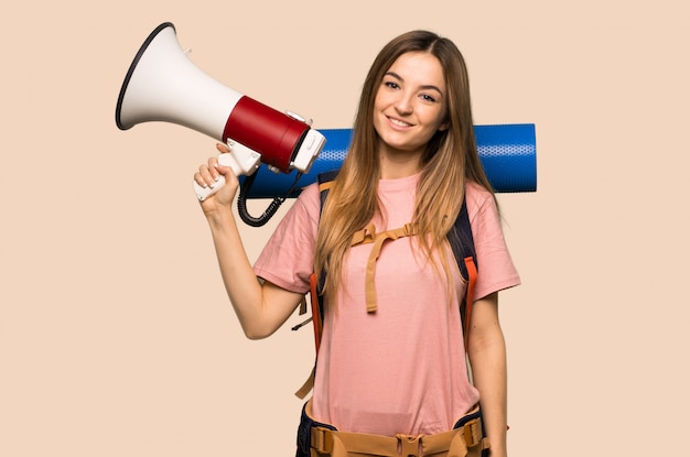 Femme jeune routard tenant un mégaphone sur fond jaune isolé