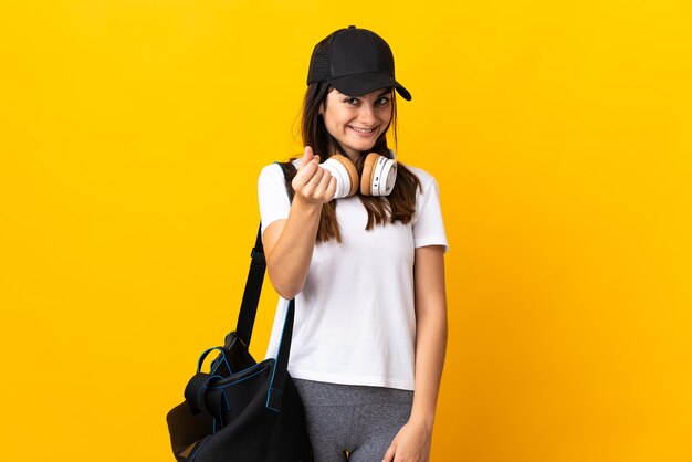 Femme jeune sport avec sac de sport isolé sur fond jaune faisant un geste d'argent