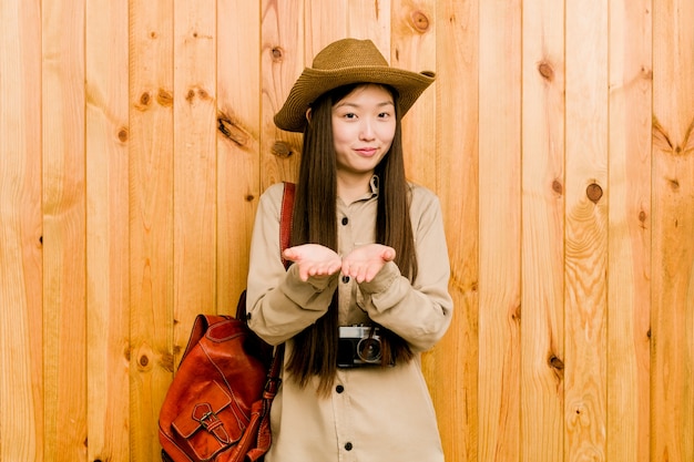 Femme jeune voyageur chinois tenant quelque chose avec des paumes, offrant à la caméra.
