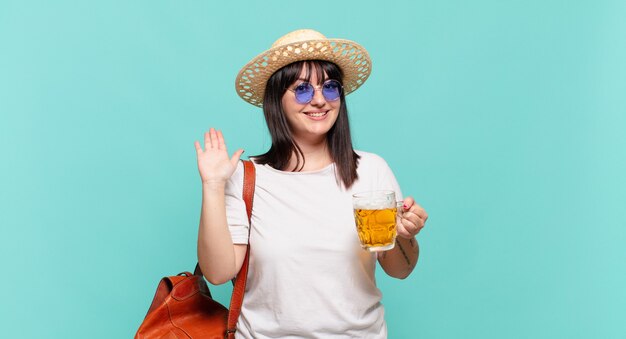 Femme jeune voyageur souriant joyeusement et gaiement, en agitant la main, en vous accueillant et en vous saluant, ou en vous disant au revoir