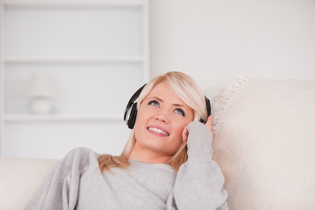 Femme jolie blonde avec un casque allongé dans un canapé