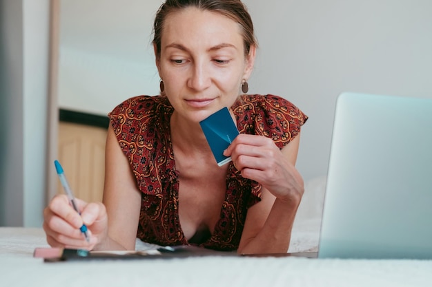 Photo une femme en jolie robe fait des notes pour une fille qui fait des achats en ligne en utilisant un ordinateur portable et une carte de crédit