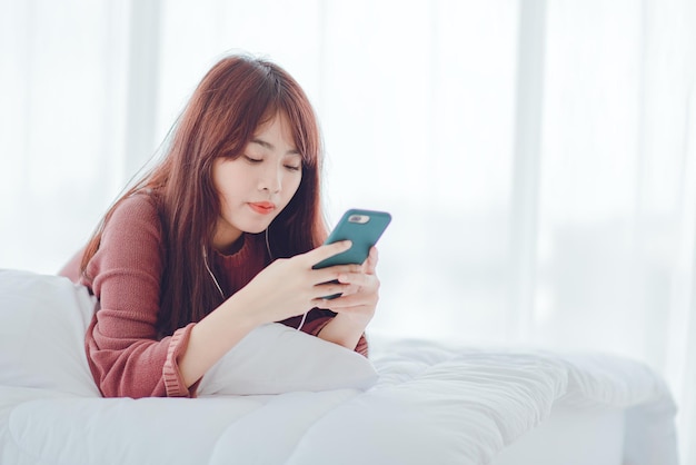 Une femme jouant au téléphone dans le lit de la maison