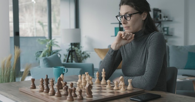 Femme jouant aux échecs à la maison elle pense et regarde l'échiquier