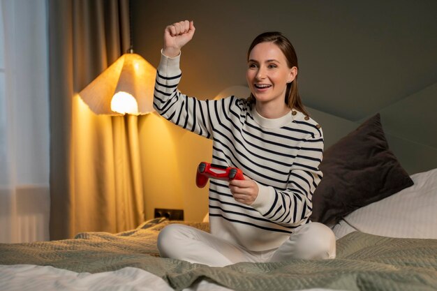 Femme jouant à des jeux vidéo avec un contrôleur de jeu tout en étant allongée dans le lit la jolie fille avait l'air excitée