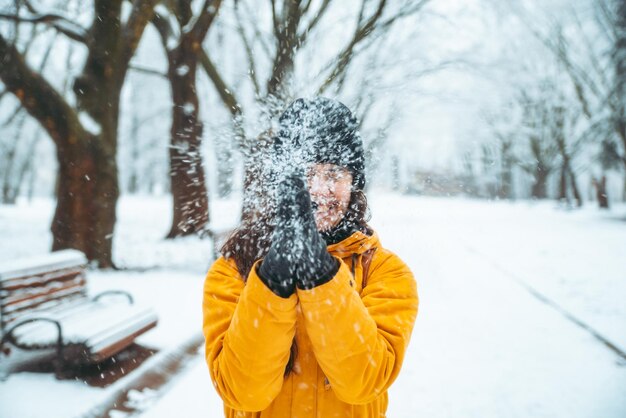 Femme jouant avec de la neige dans le parc de la ville enneigée