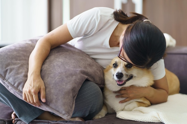 Une femme jouant avec son chien à la maison, un adorable corgi sur le canapé dans le salon.
