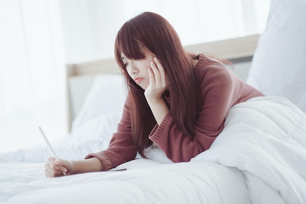 Une femme jouant une tablette sur le lit dans une chambre blanche