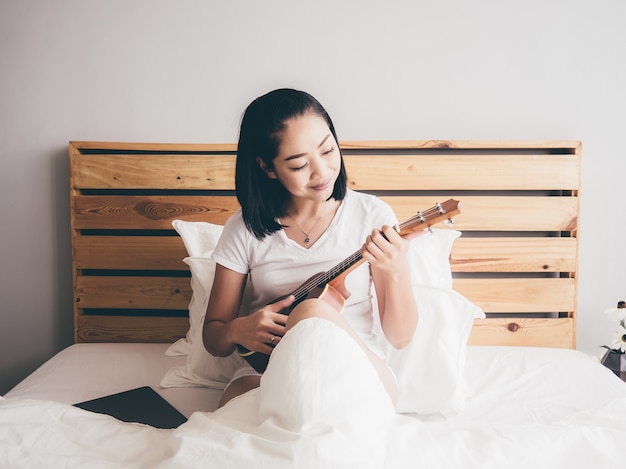 Une femme joue du ukulele sur son lit le matin.