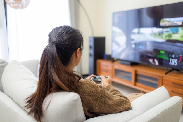 Une femme joue à un jeu vidéo et s'assoit sur le canapé à la maison.