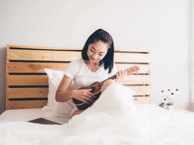 Femme joue ukulélé sur son lit le matin.