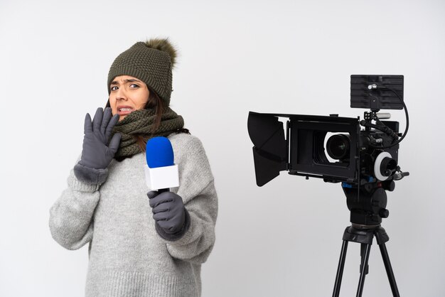 Femme journaliste tenant un microphone et rapportant des nouvelles sur fond blanc isolé nerveux étirant les mains vers l'avant