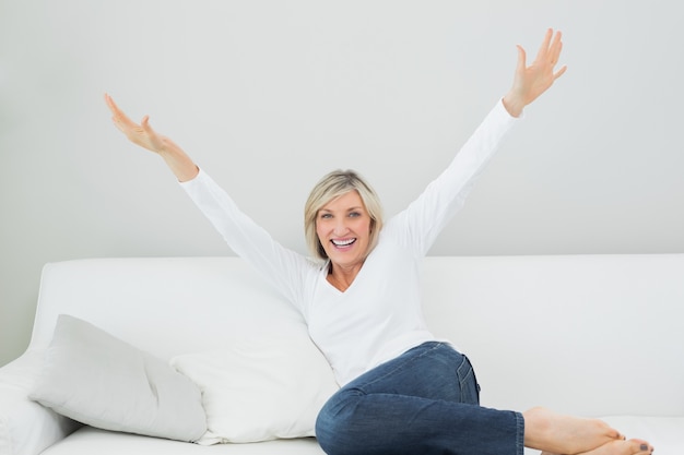 Photo femme joyeuse, assis sur le canapé avec les bras tendus à la maison